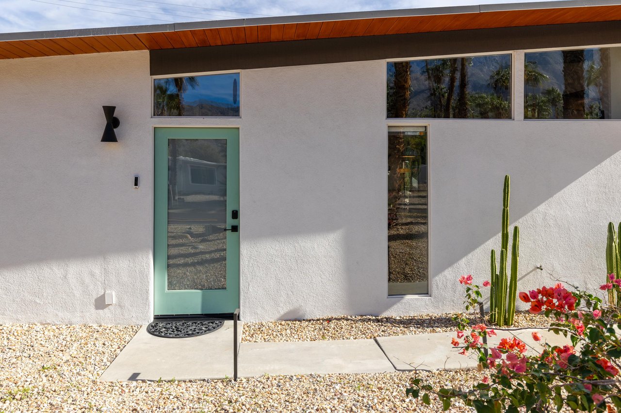Modern desert property featuring clean architectural lines, striking turquoise entry door, and desert landscaping with blooming bougainvillea.