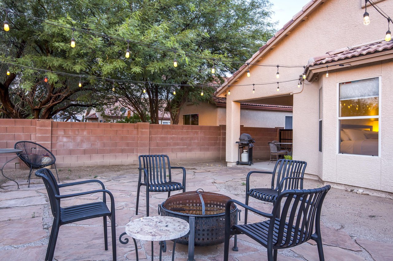 Cozy outdoor space with string lights, fire pit, covered patio, and outdoor seating.
