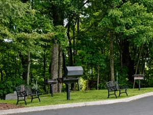The property is nestled in a peaceful wooded setting with mature trees, featuring outdoor grilling facilities and decorative seating areas throughout the landscaped grounds.