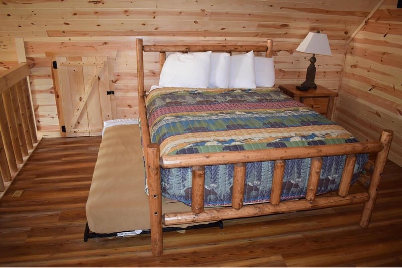 Cozy log cabin bedroom with handcrafted wooden bed and colorful quilt awaits your peaceful mountain retreat.