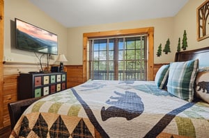 Cozy cabin bedroom with rustic wood walls, mountain quilt, and peaceful forest views through your window.