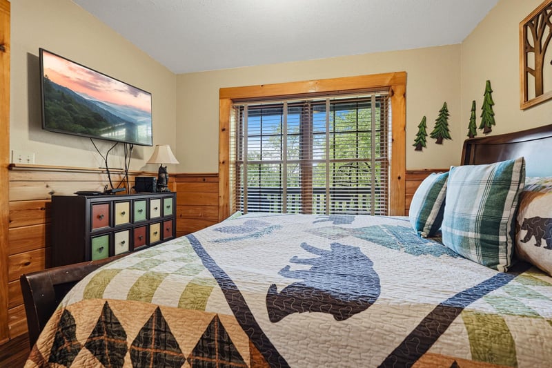 Cozy cabin bedroom with rustic wood walls, mountain quilt, and peaceful forest views through your window.