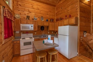 Kitchen with white appliances and breakfast bar with seating for two at Logans Smoky Den, a 2 bedroom cabin rental located in Pigeon Forge
