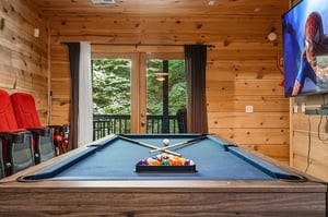 Challenge your friends to a billiards match in this cozy game room, where rustic wood walls and forest views create the perfect retreat for friendly competition.