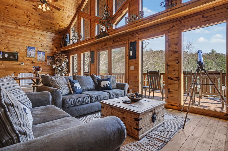 Unwind in your cozy cabin living room where plush sofas await after mountain adventures. Large windows frame forest views.
