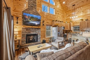 Your cozy cabin retreat features warm wood walls, stone fireplace, and open kitchen—perfect for unwinding after mountain adventures.