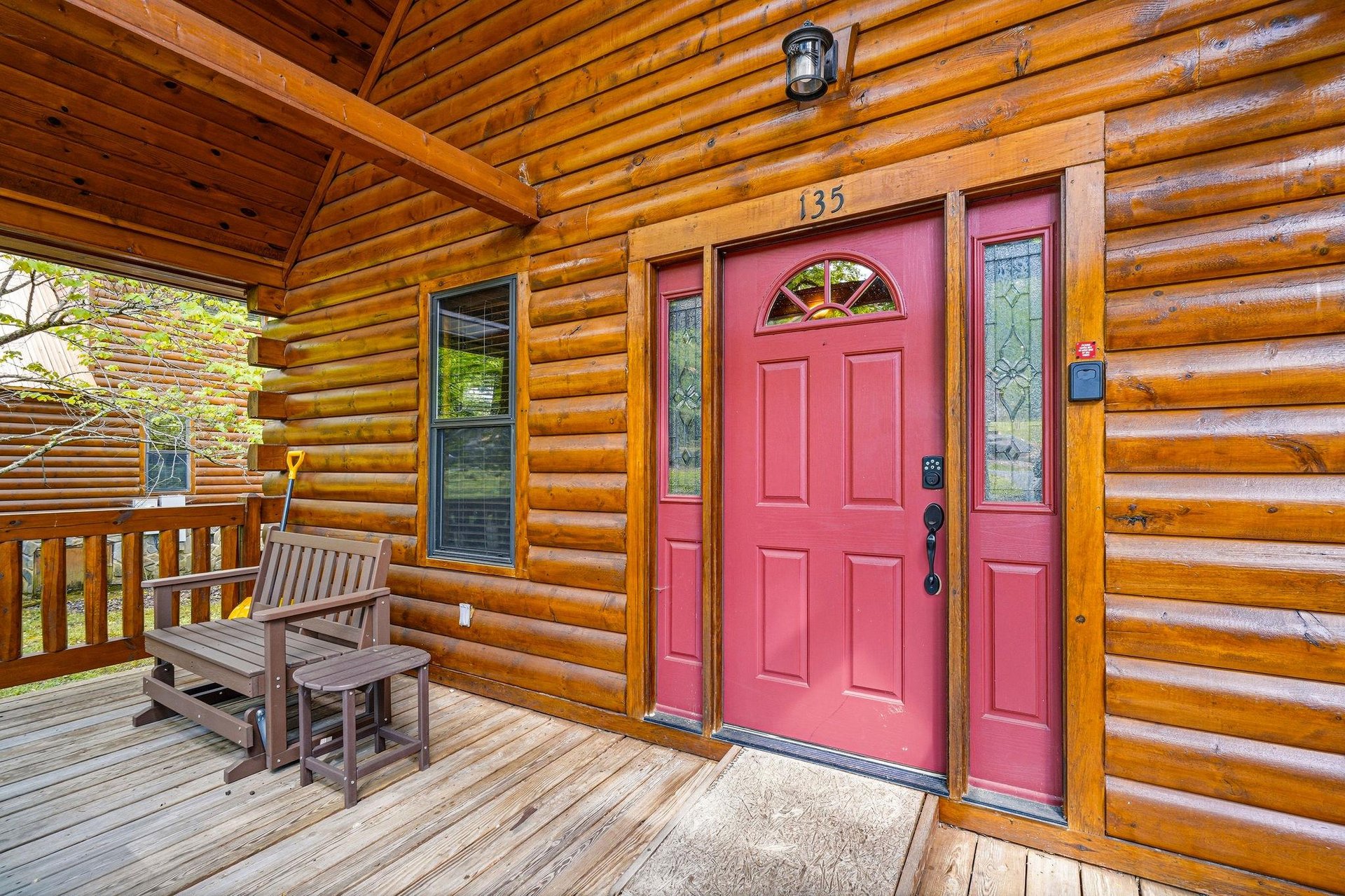 Step onto your welcoming wooden deck where the charming red door beckons you into your cozy log cabin retreat.