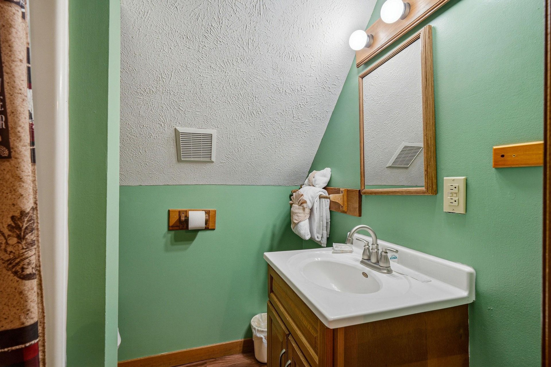 Freshen up in your charming bathroom featuring mint green walls, warm wood vanity, and thoughtful touches like fluffy towels.