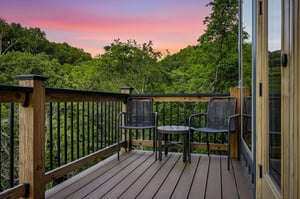 A tranquil deck overlooking lush forest views at sunset, where the sky glows pink and orange over the trees—a serene backdrop for morning coffee or evening relaxation in the fresh air.