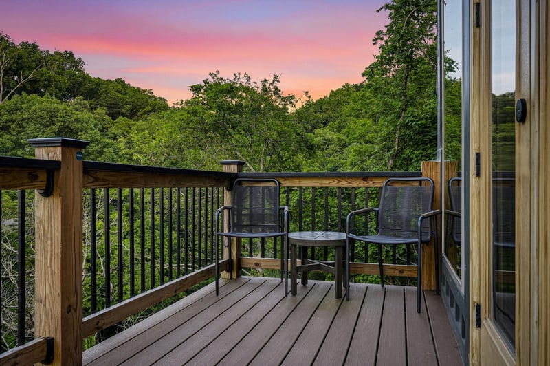 A tranquil deck overlooking lush forest views at sunset, where the sky glows pink and orange over the trees—a serene backdrop for morning coffee or evening relaxation in the fresh air.