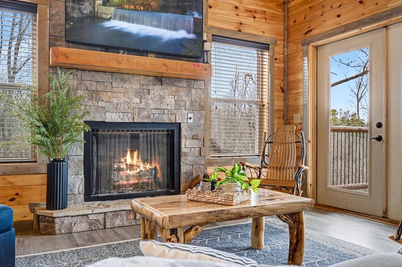 Curl up by your crackling stone fireplace in this cozy living room, where rustic wood beams and warm flames create the perfect retreat.
