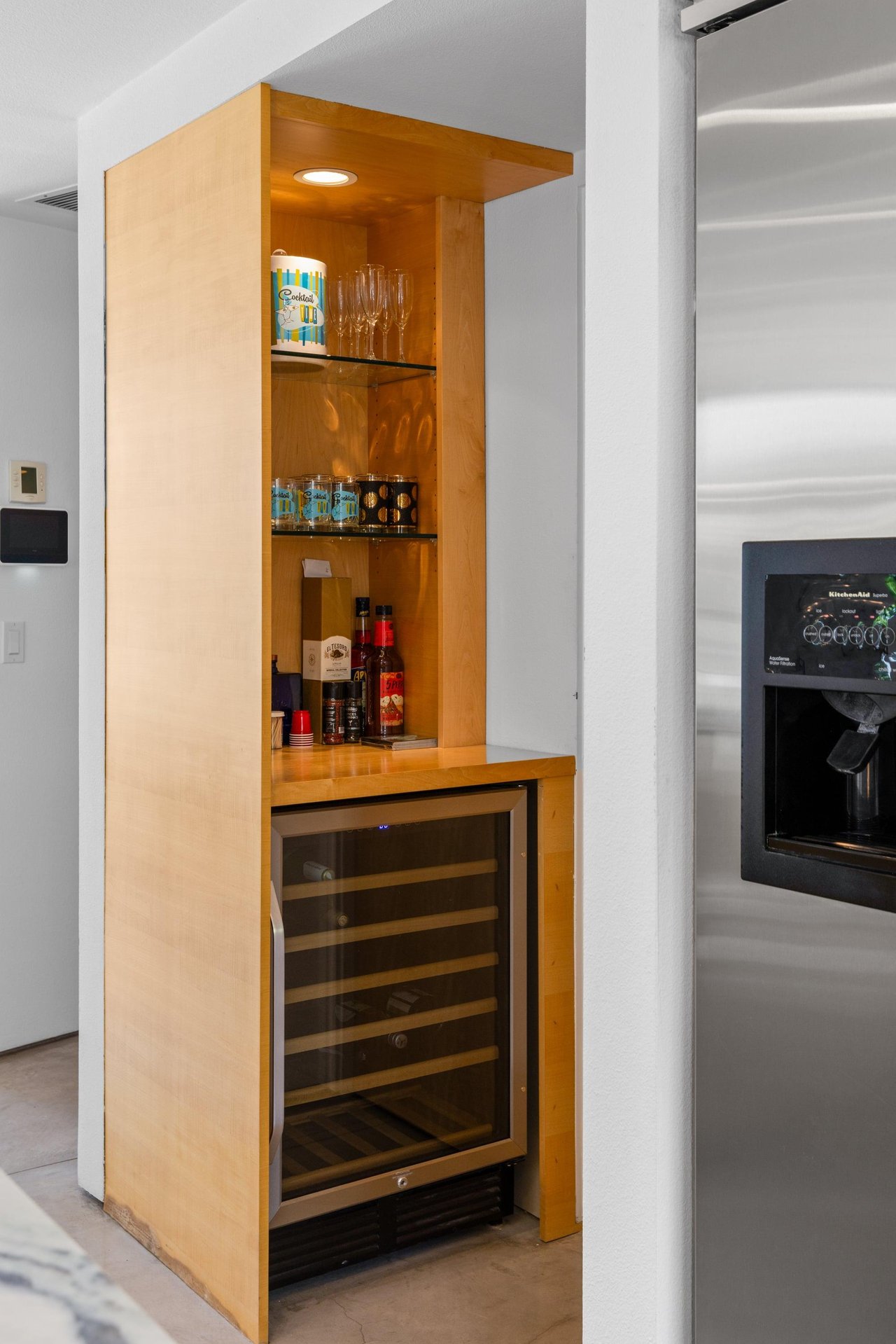 Modern chefs kitchen with a waterfall marble counter, kitchen island, stainlesssteel appliances, wine fridge, wet bar, and kitchen essentials.