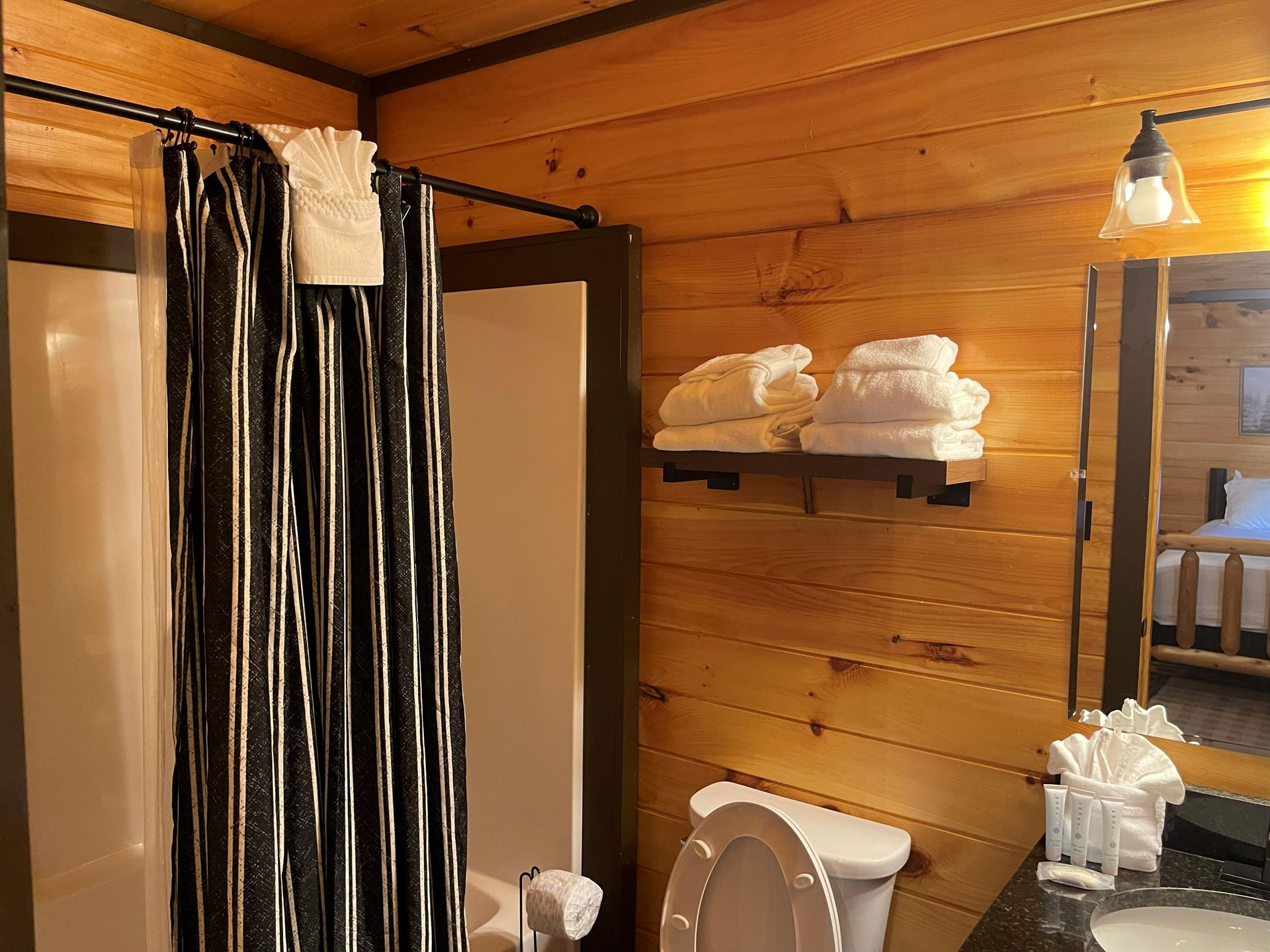 Step into a cozy cabinstyle bathroom where rustic wood walls meet modern comfort. Fresh towels await on the shelf, and thoughtful amenities are ready for you.