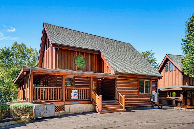 The property features a warm wooden exterior with covered porches and mountainstyle architecture, nestled among tall trees in a peaceful wooded setting.