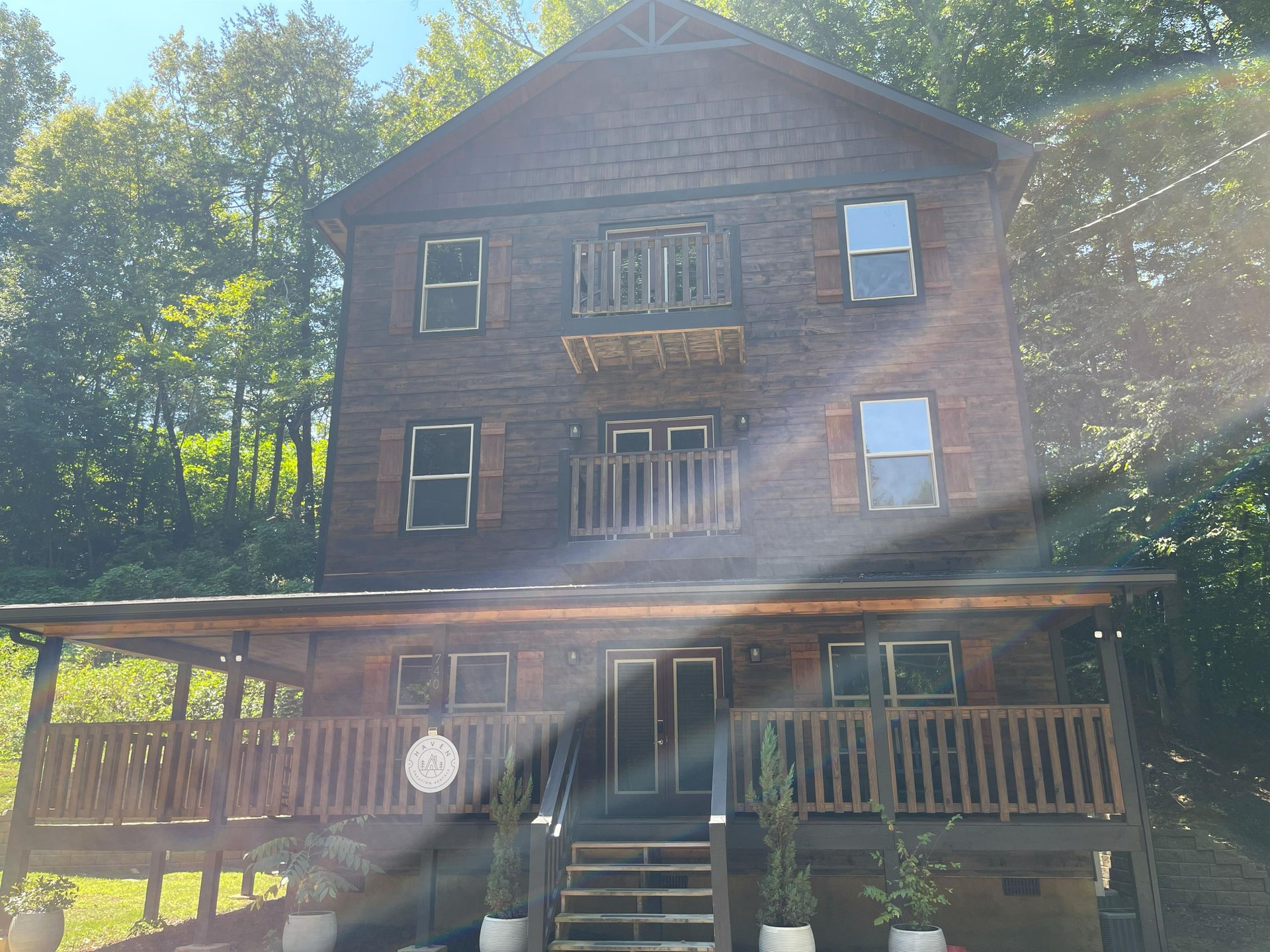 Threestory woodsided chalet featuring multiple balconies and surrounded by tall trees in a peaceful forest setting.