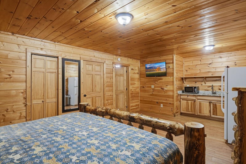 Relax in your cozy log cabin bedroom with rustic charm, featuring a handcrafted log bed and convenient kitchenette for mountain getaway comfort.