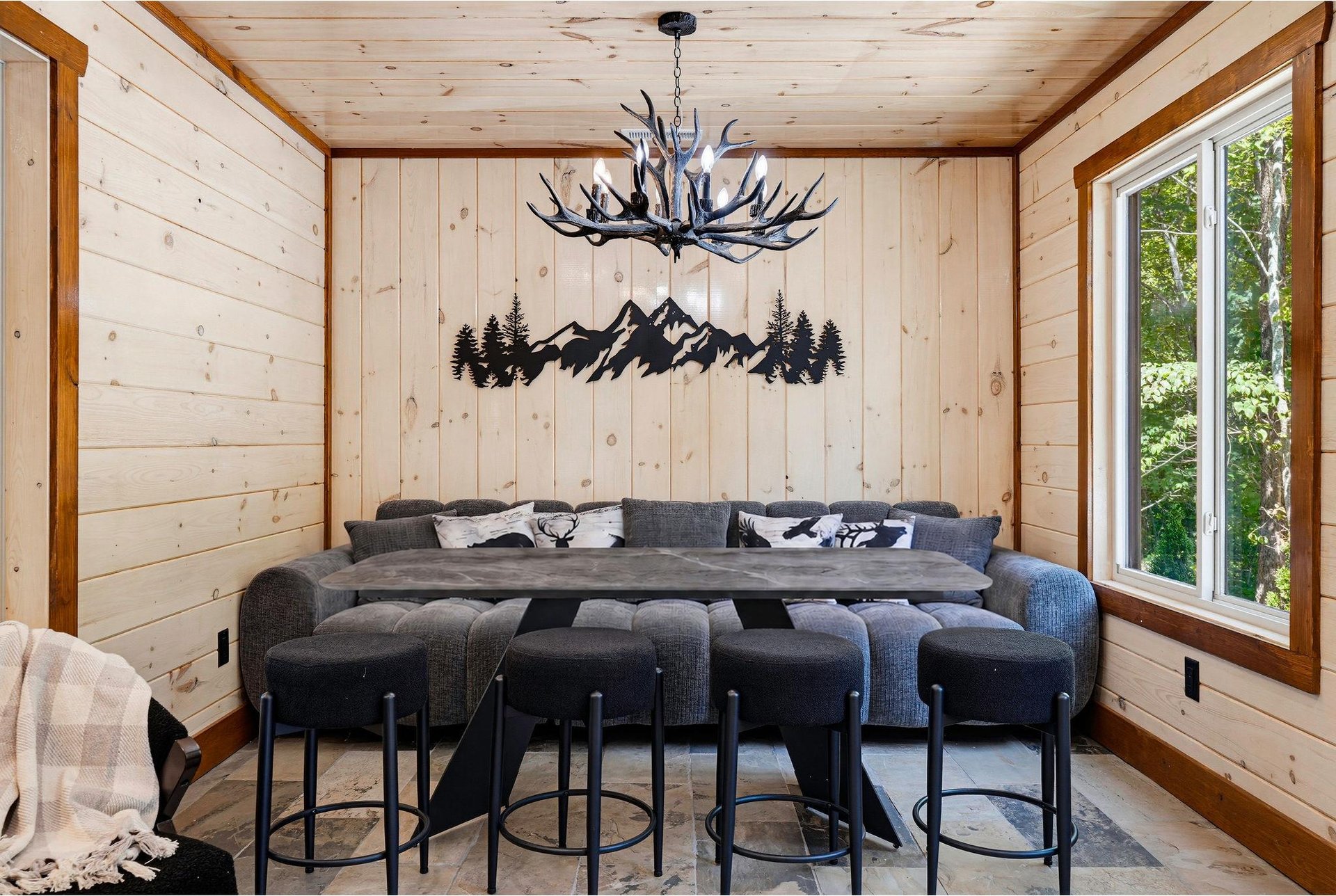 Curl up in this cozy living room, where rustic wood paneling, a striking antler chandelier, and mountaininspired decor create the perfect alpine retreat for your group.