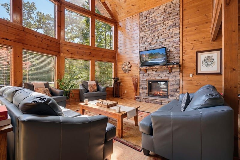 Picture yourself unwinding in this sunlit great room, where vaulted wood ceilings and floortoceiling windows frame peaceful forest views. Cozy leather seating encircles a warm stone fireplace, invit