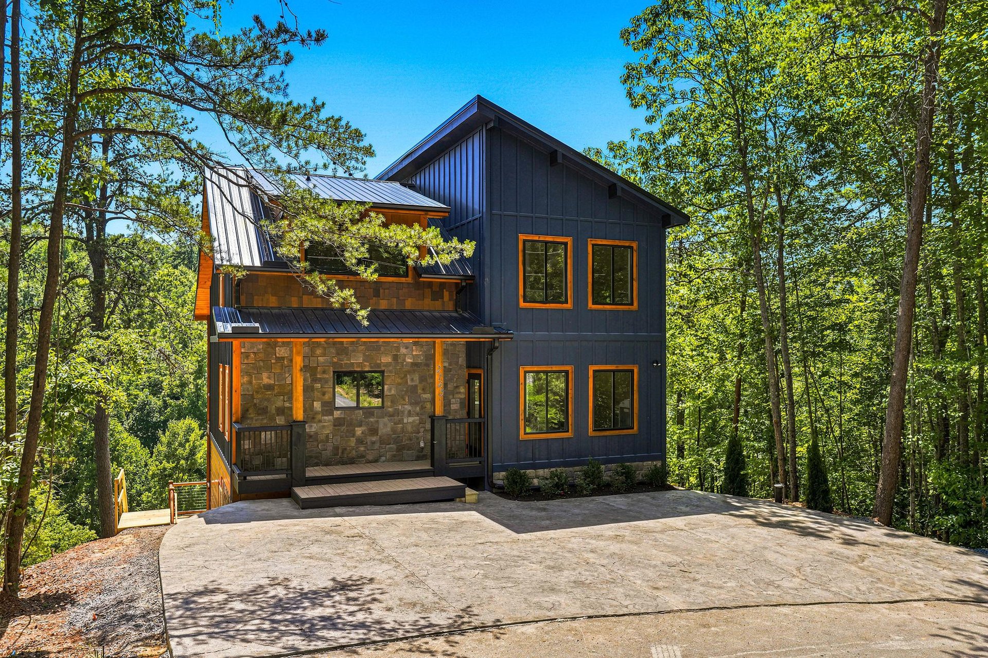 Modern twostory retreat nestled among towering trees, featuring striking dark wood siding with warm orange trim and spacious decks for enjoying the surrounding forest.