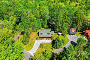 Aerial view of a secluded forest property with spacious driveway and lush woodland surroundings.