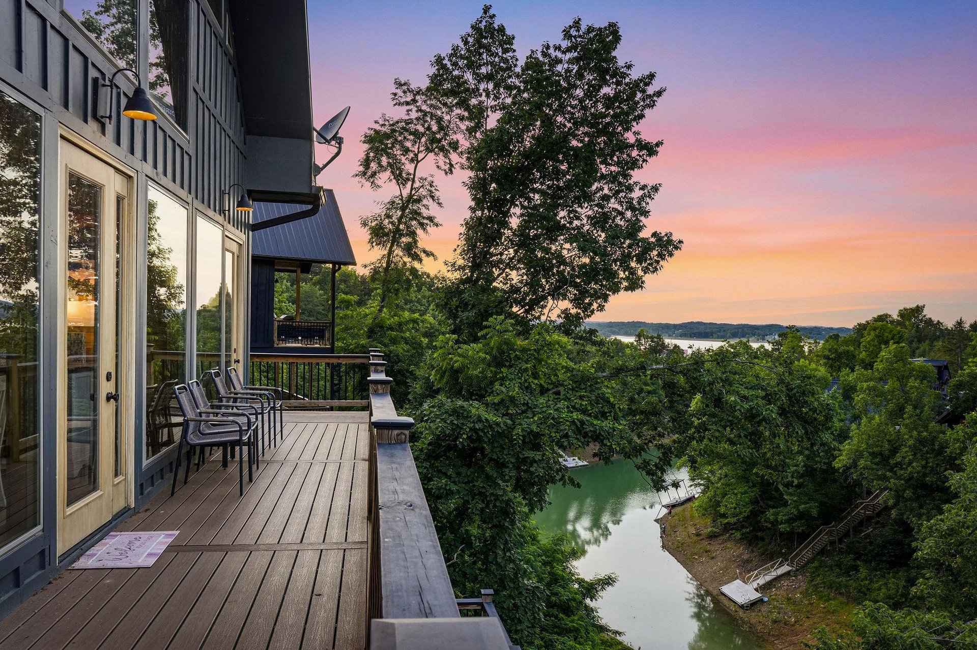 Stunning sunset paints the sky over a peaceful waterfront setting, with a deck overlooking lush greenery and tranquil lake views nestled in the surrounding landscape.