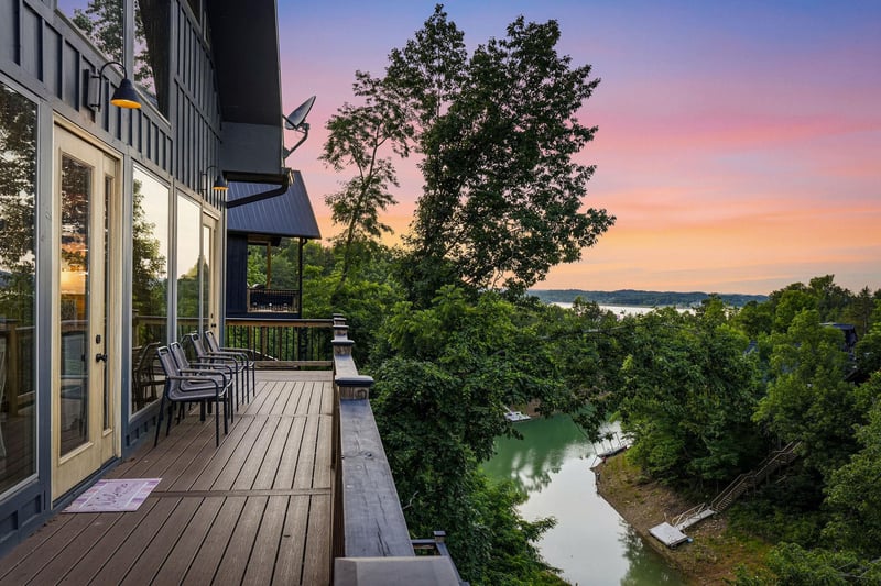 Stunning sunset paints the sky over a peaceful waterfront setting, with a deck overlooking lush greenery and tranquil lake views nestled in the surrounding landscape.