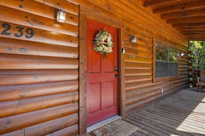 Charming log cabin entrance with rustic red door and welcoming wreath—your mountain retreat awaits behind this inviting facade.