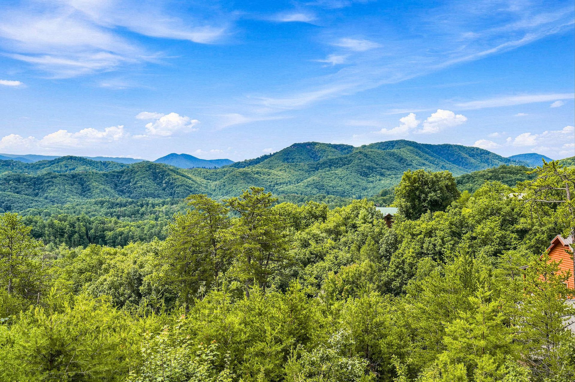 Stunning panorama of rolling green mountains stretching to the horizon under bright blue skies, with the property nestled among lush forest.