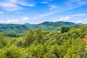 Stunning panorama of rolling green mountains stretching to the horizon under bright blue skies, with the property nestled among lush forest.