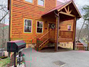 Charming log cabin exterior with covered porch and outdoor grilling station for your mountain getaway.