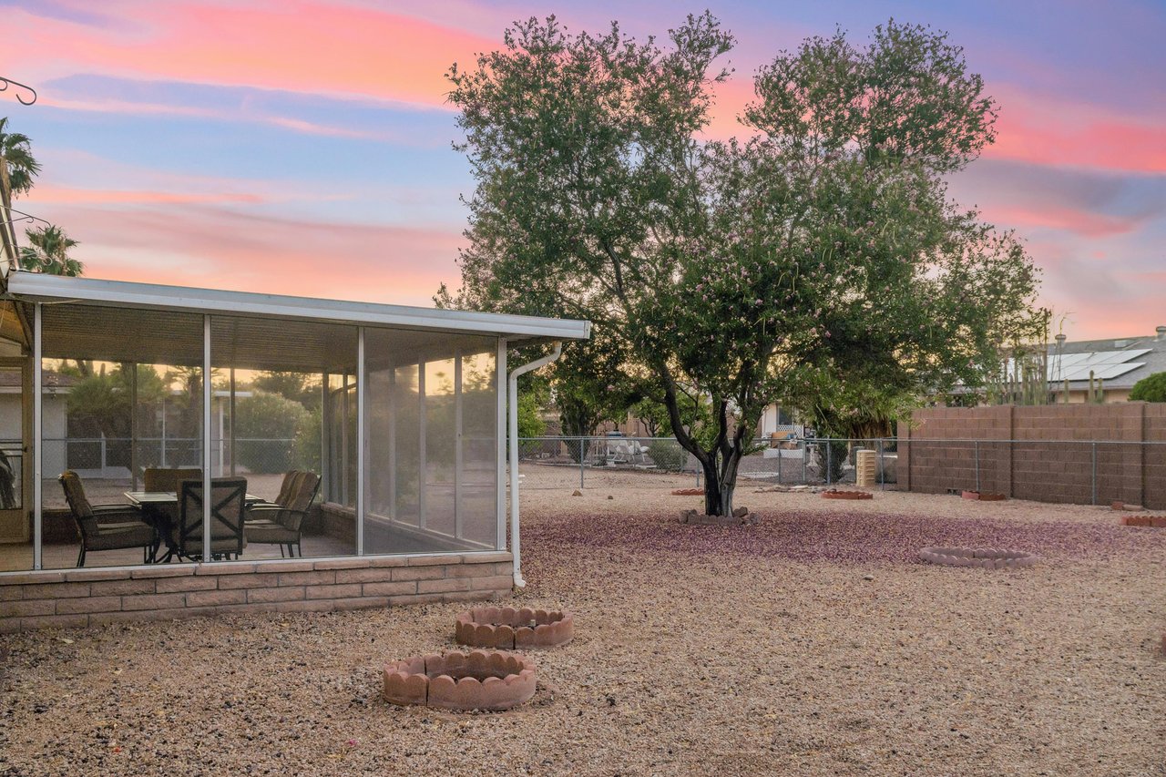Large outdoor space in backyard with BBQ, additional table, and fencedin yard.