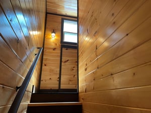 Warm wood paneling lines the stairwell, drawing your eye upward to the natural light streaming through the tall windows above.