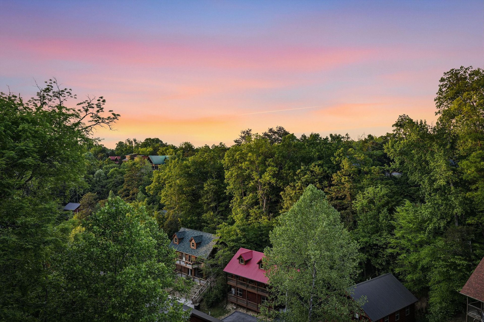 Stunning sunset paints the sky in vibrant hues above this peaceful forested neighborhood, creating a picturesque backdrop for your mountain retreat.