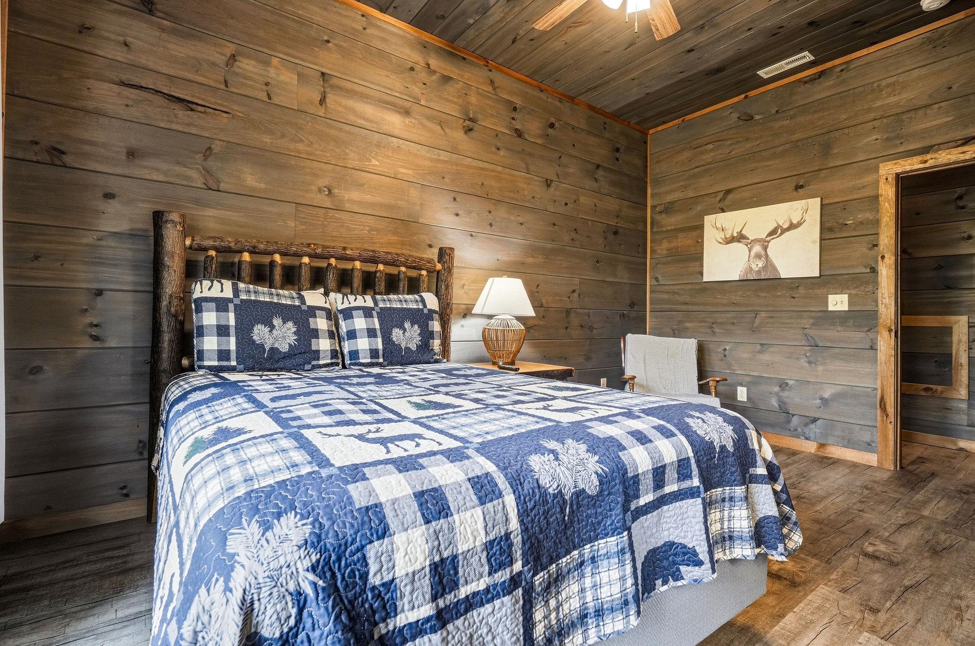 Sink into your cozy retreat surrounded by rustic wood walls, where a handcrafted log bed and charming blue plaid quilt invite you to unwind after a day of mountain adventures.