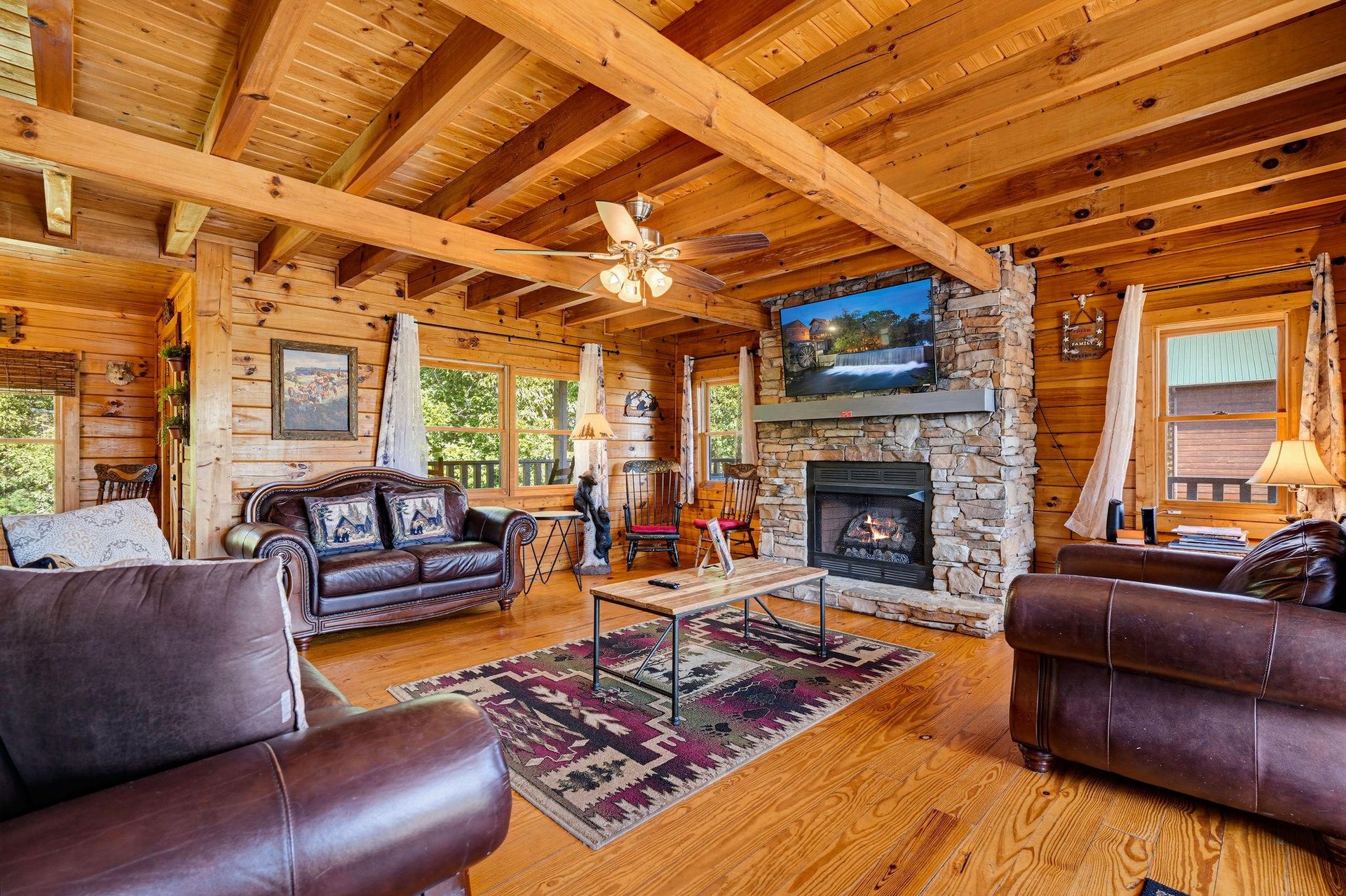Gather under soaring timber beams in your spacious cabin retreat, where rich leather seating and a stunning stone fireplace create the perfect spot to unwind after exploring the mountains.