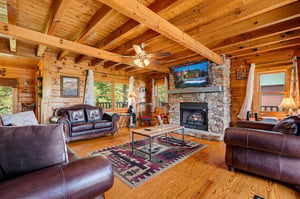 Gather under soaring timber beams in your spacious cabin retreat, where rich leather seating and a stunning stone fireplace create the perfect spot to unwind after exploring the mountains.