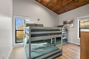 A cozy bedroom where rustic wood ceilings meet modern comfort. Your crew will love the bunk beds while you enjoy peaceful views of autumn foliage through the generous windows.