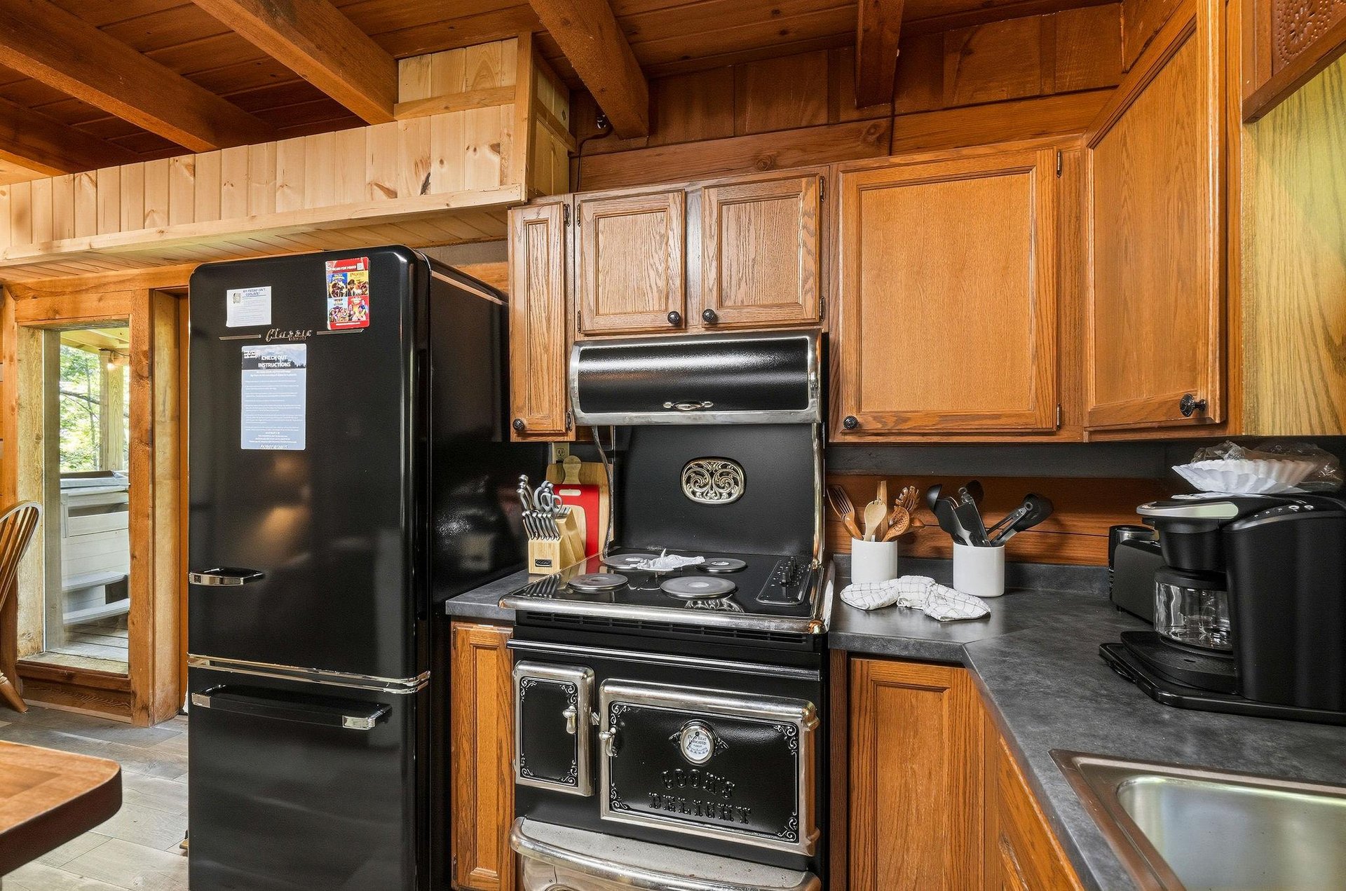 Your wellappointed kitchen features a striking vintagestyle stove and modern refrigerator, set within charming woodpaneled walls and exposed beam ceilings that create a warm cabin atmosphere for yo