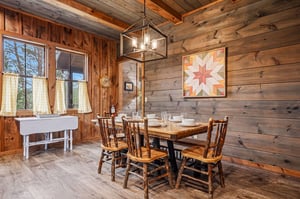 Gather around this warm wooden table beneath a modern chandelier. Sunlight filters through cafe curtains, illuminating cozy rustic walls and a welcoming space perfect for your morning coffee.