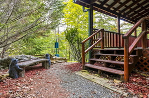 A rustic wooden deck extends into a tranquil forest setting, where carved bear sculptures and mosscovered logs blend with the surrounding trees—a peaceful place to step outside and feel truly immerse