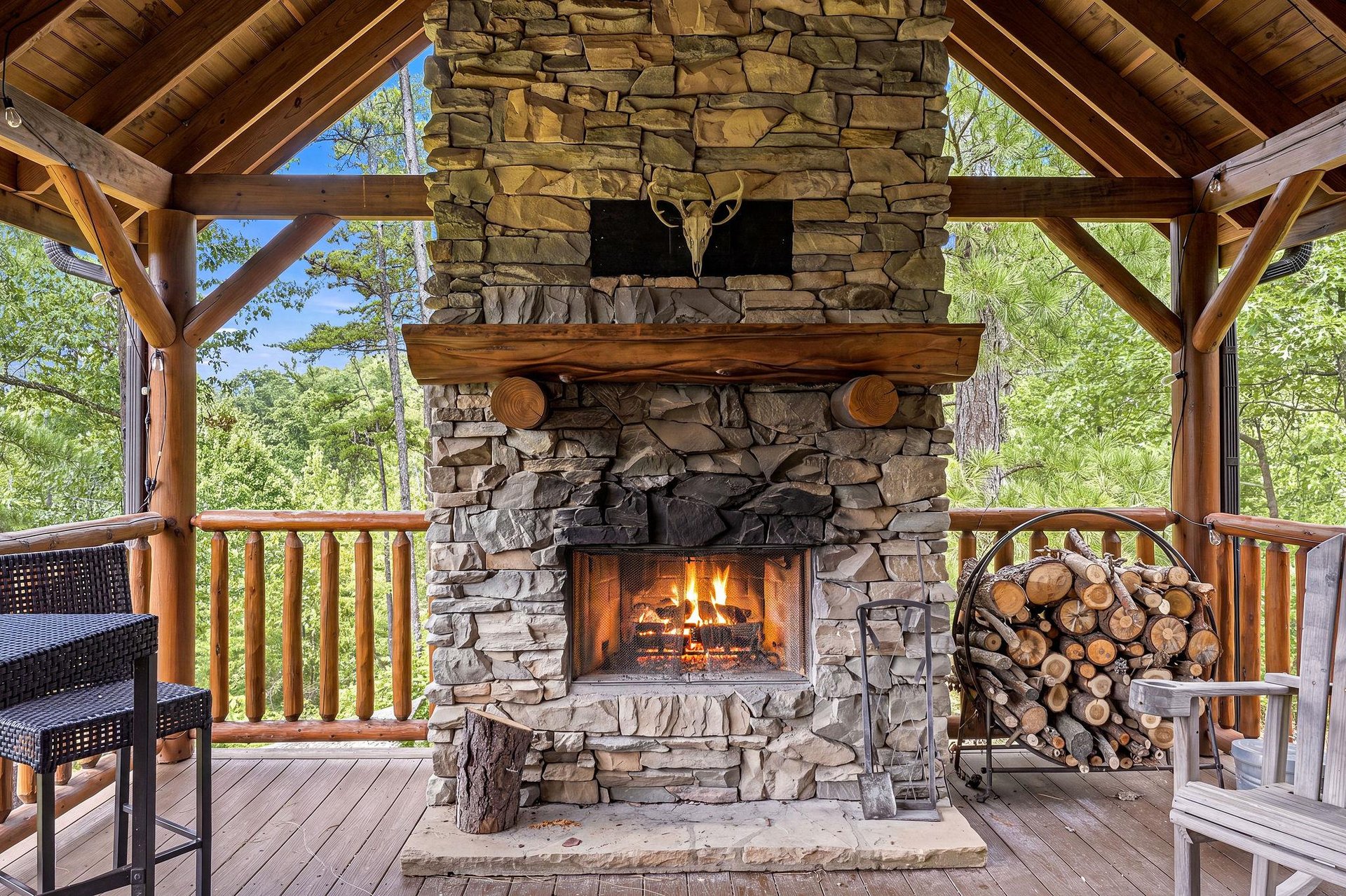 Gather around the inviting outdoor fireplace on the covered terrace, where rustic stonework and warm flames meet views of lush greenery—your perfect mountain retreat awaits.
