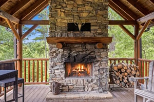 Gather around the inviting outdoor fireplace on the covered terrace, where rustic stonework and warm flames meet views of lush greenery—your perfect mountain retreat awaits.