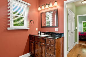 Freshen up in your private bathroom featuring warm terracotta walls, elegant vanity lighting, and a sleek black countertop with wooden cabinetry offering plenty of storage for all your essentials.