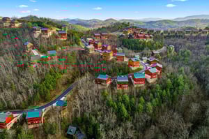 Mountain resort community nestled among rolling hills and forested valleys, featuring colorful cabins and scenic winding roads.