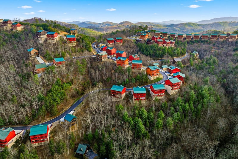 Mountain resort community nestled among rolling hills and forested valleys, featuring colorful cabins and scenic winding roads.