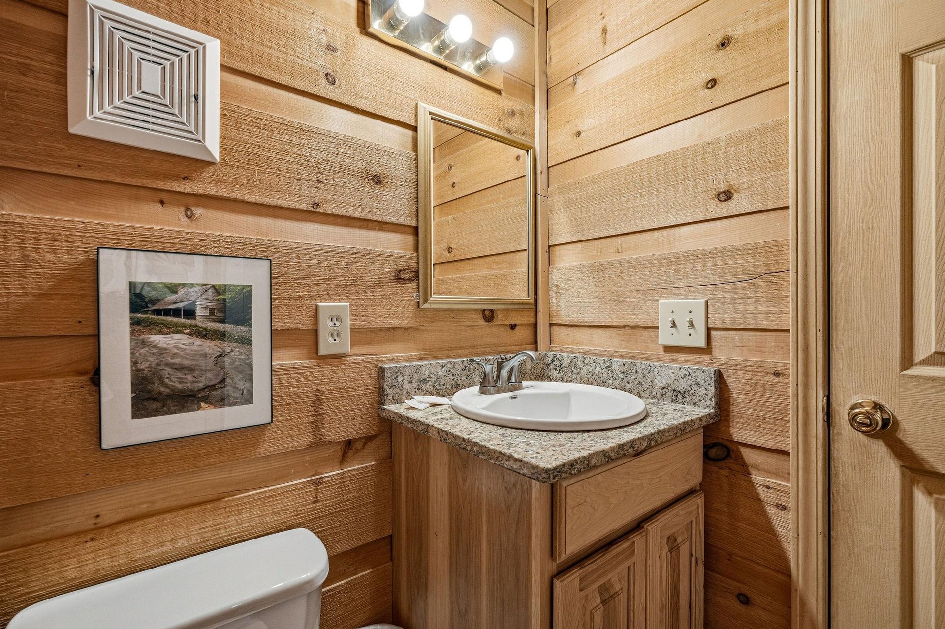 Your private bathroom features rustic wood paneling, granite countertops, and warm lighting—a cozy retreat after a day of mountain adventures.