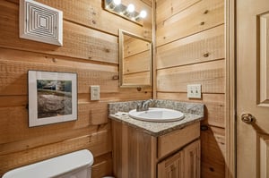 Your private bathroom features rustic wood paneling, granite countertops, and warm lighting—a cozy retreat after a day of mountain adventures.