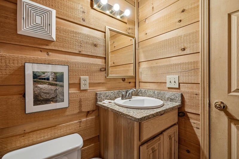 Your private bathroom features rustic wood paneling, granite countertops, and warm lighting—a cozy retreat after a day of mountain adventures.