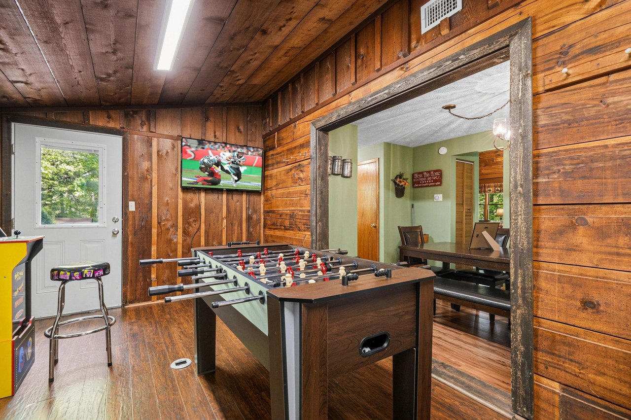 Your private game room features foosball, arcade games, and a mounted TV in rustic wood surroundings for endless entertainment.