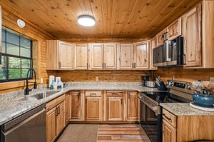 Cook your favorite meals in this charming full kitchen featuring warm wood cabinetry, granite countertops, and modern appliances in a cozy cabin setting.